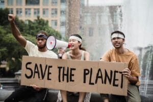 Diverse activists holding placard and megaphone at outdoor protest for climate action.