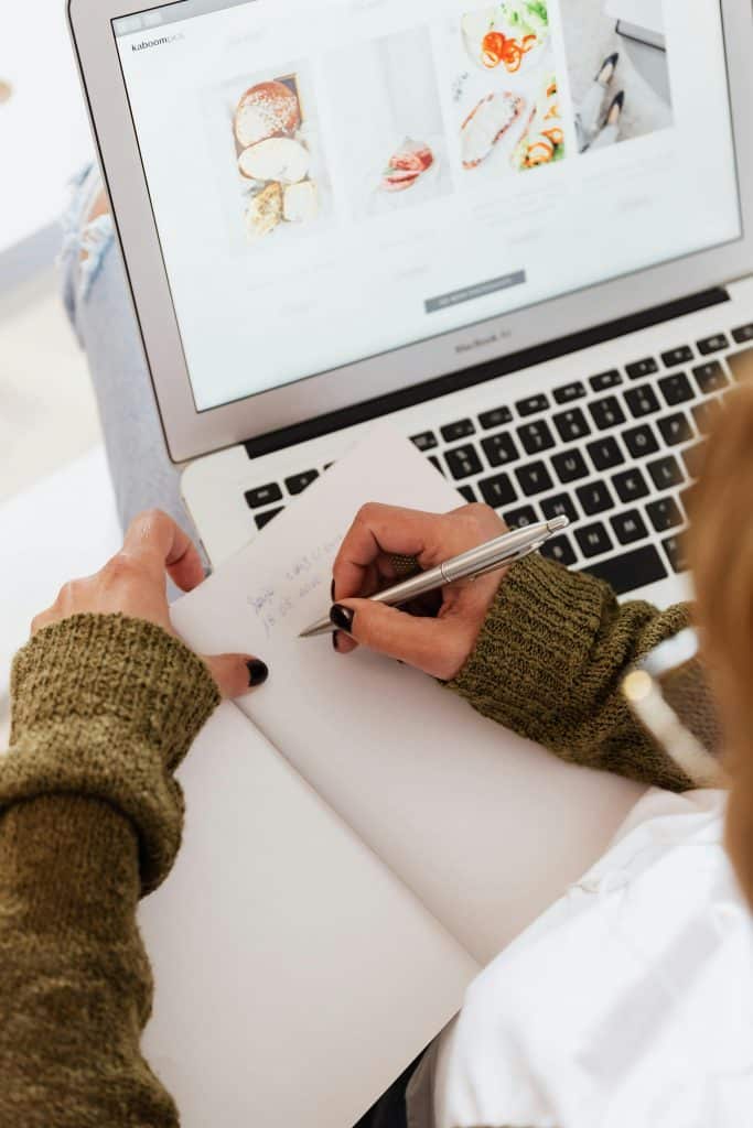 pexels-photo-4468011-4468011 Overhead view of a woman writing in a notebook while browsing on a laptop.