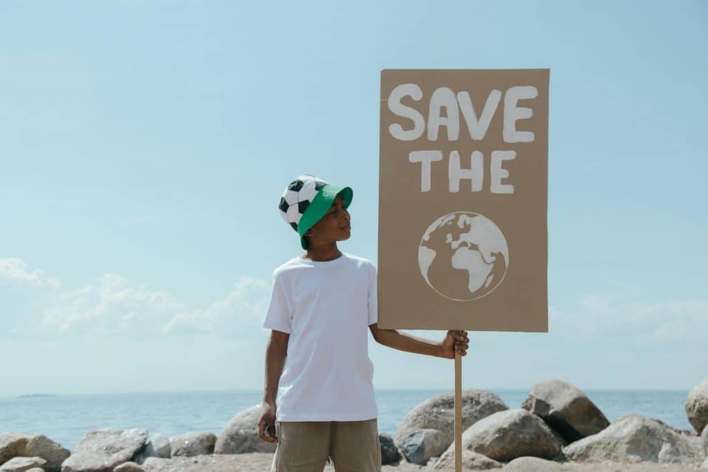 pexels-photo-8989995-8989995 Young boy at beach holding a sign promoting environmental awareness and earth conservation.