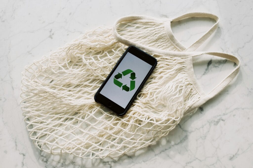 pexels-photo-3850512-3850512 Overhead of smartphone with simple recycling sign on screen placed on white eco friendly mesh bag on marble table in room
