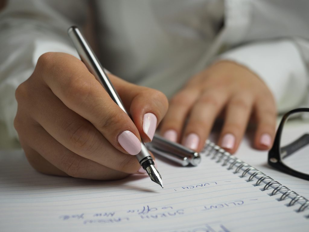 pexels-photo-110473-110473 A detailed image of handwriting in a notebook with a fountain pen and glasses, ideal for office themes.