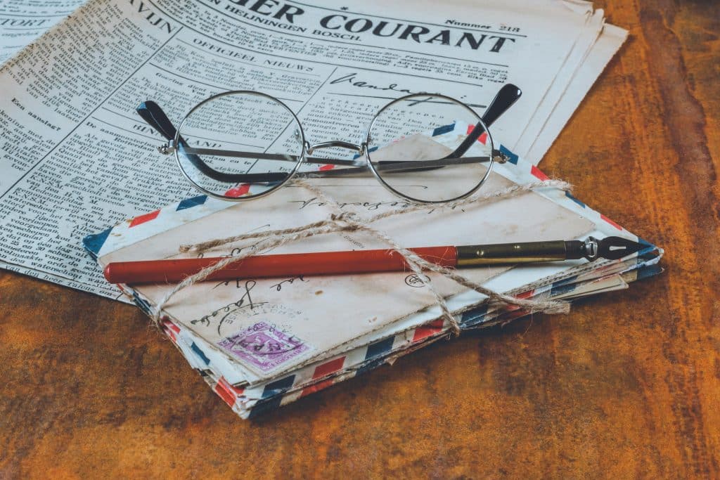 pexels-photo-1809342-1809342 Historical letters and a fountain pen on a vintage wooden table, alongside eyeglasses and a newspaper.