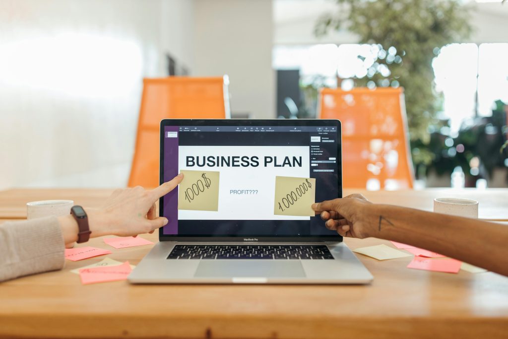 pexels-photo-7278886-7278886 Two professionals strategizing a business plan on a laptop with sticky notes and profit goals.